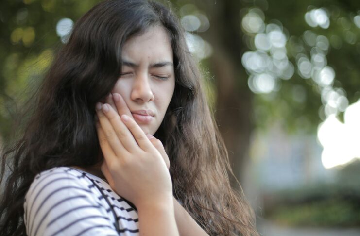 Portrait of a young woman feeling toothache, showing discomfort outdoors with a pained facial expression.