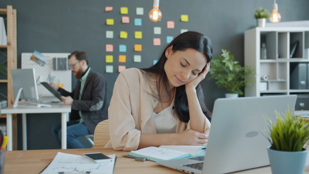 A woman resting her head on her hand at a desk, looking bored.