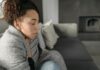 Employers ‘Failing to Track Sickness Absence Impact’ Young woman resting at home, wrapped in a blanket and feeling unwell, conveying a sense of illness or discomfort.