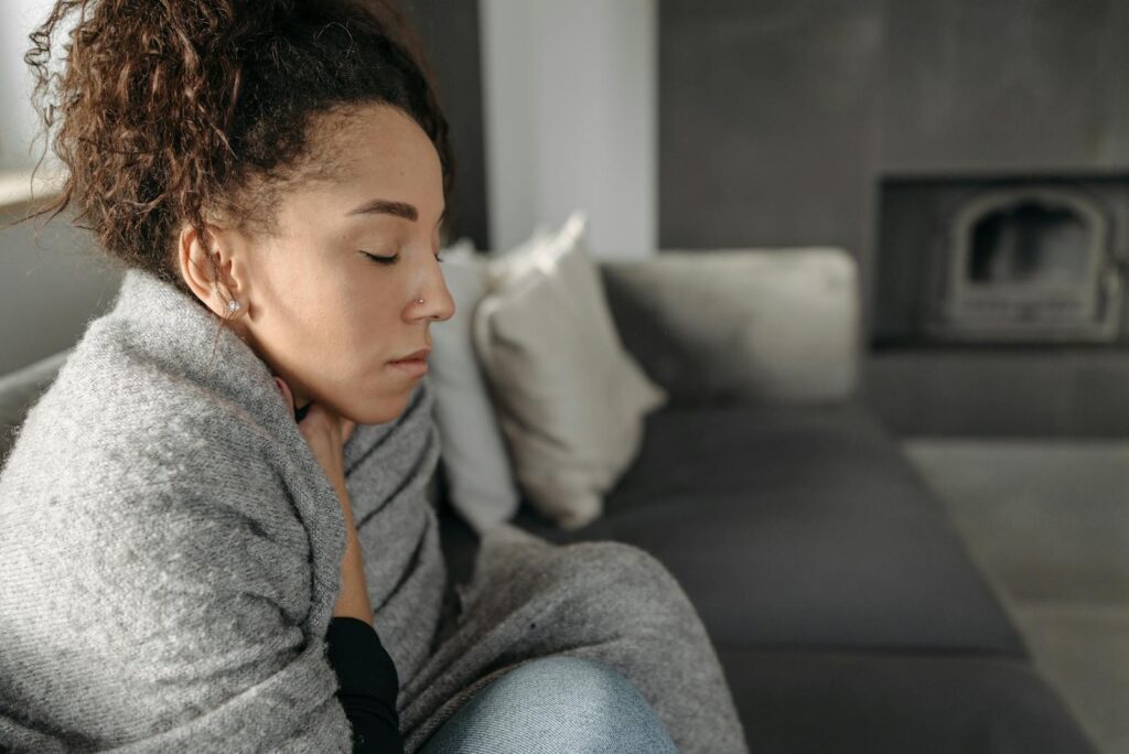 Young woman resting at home, wrapped in a blanket and feeling unwell, conveying a sense of illness or discomfort.