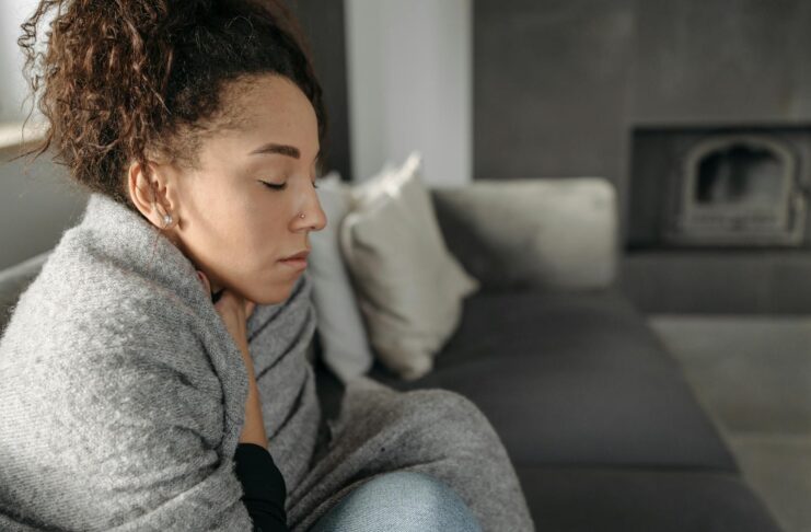 Young woman resting at home, wrapped in a blanket and feeling unwell, conveying a sense of illness or discomfort.