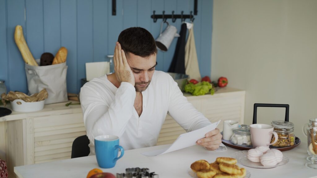 A man sitting at a table looking worried while looking at a bill.