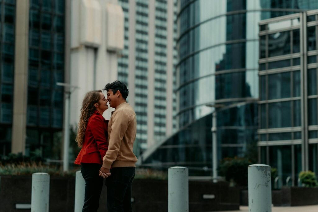 A man and woman about to kiss in front of office buildings.