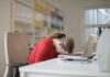 Poor Sleep Leaves UK Workers Struggling to Focus at Work A tired woman in a red sweater leans her head on a desk with a laptop, symbolizing workplace fatigue.