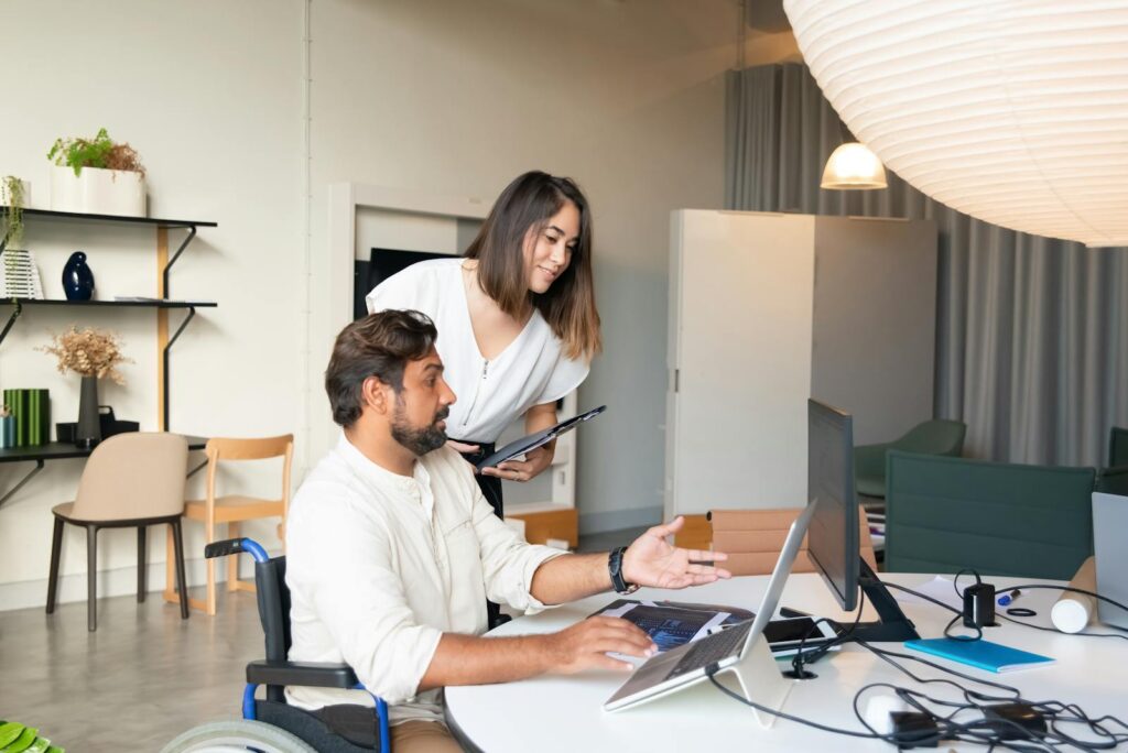 A man in a wheelchair and a woman at an office desk.