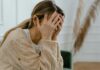 Over 1 Million Young UK Workers ‘Experience Quarter-Life Crisis’ A woman sitting indoors covering her face in despair.