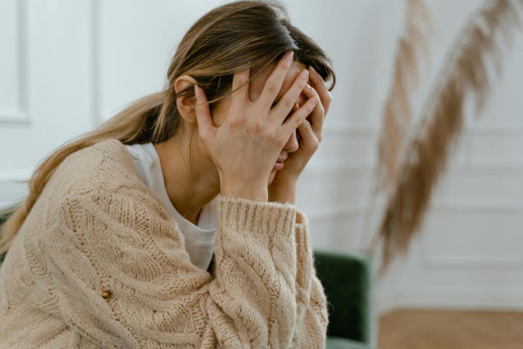 A woman sitting indoors covering her face in despair.