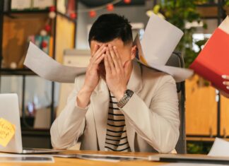Britain ‘Has Entered a Coping Era at Work’ As Employers Miss Key Warning Signs A stressed office worker overwhelmed by paperwork in office environment, demonstrating burnout.