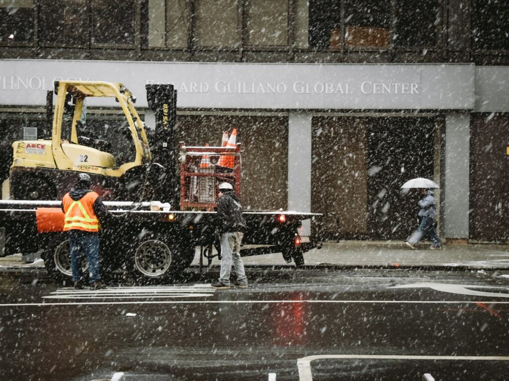 Workers with a forklift during snowfall on a city street.